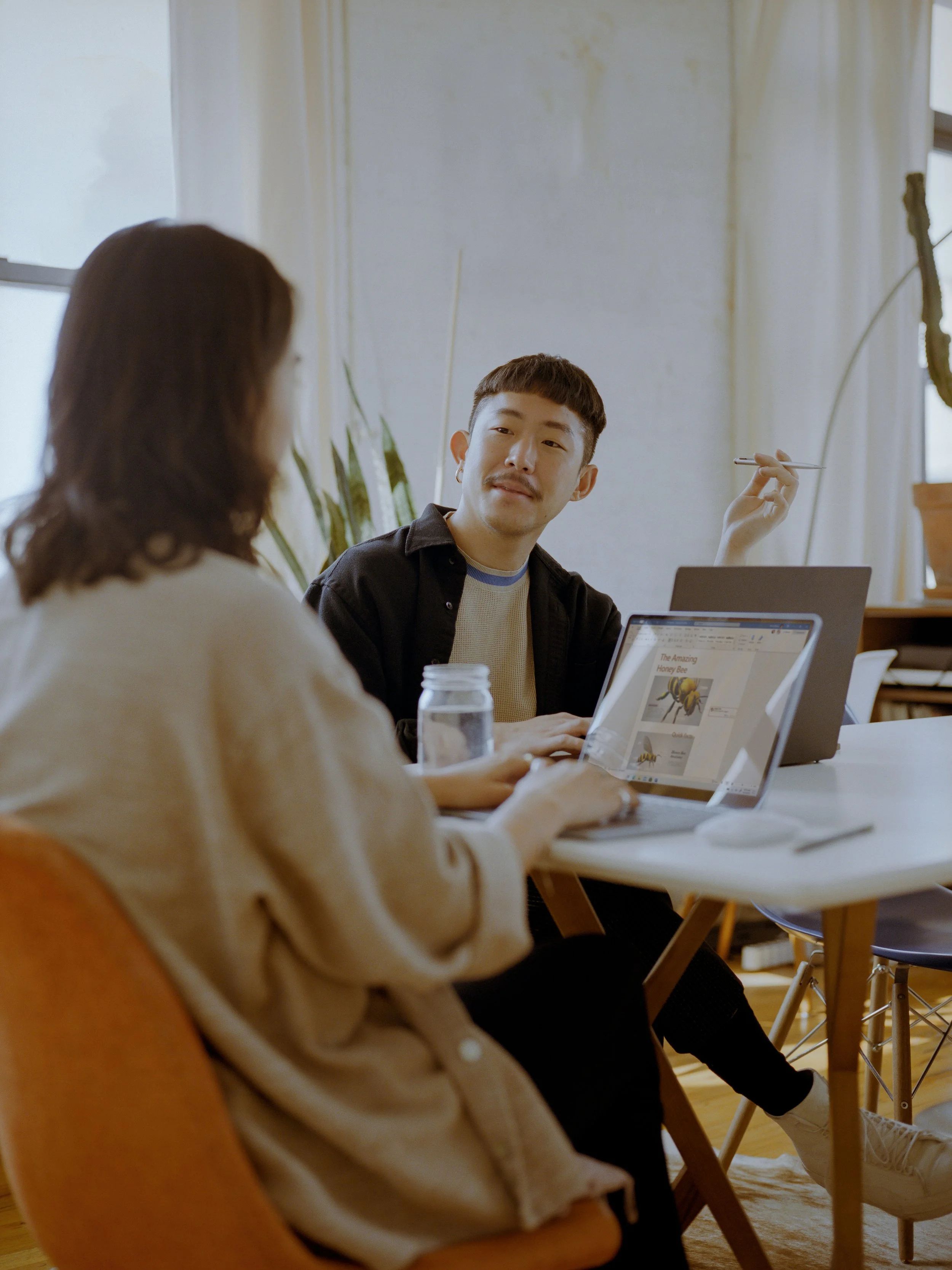 Two people sitting at a table in an office, looking at laptops.