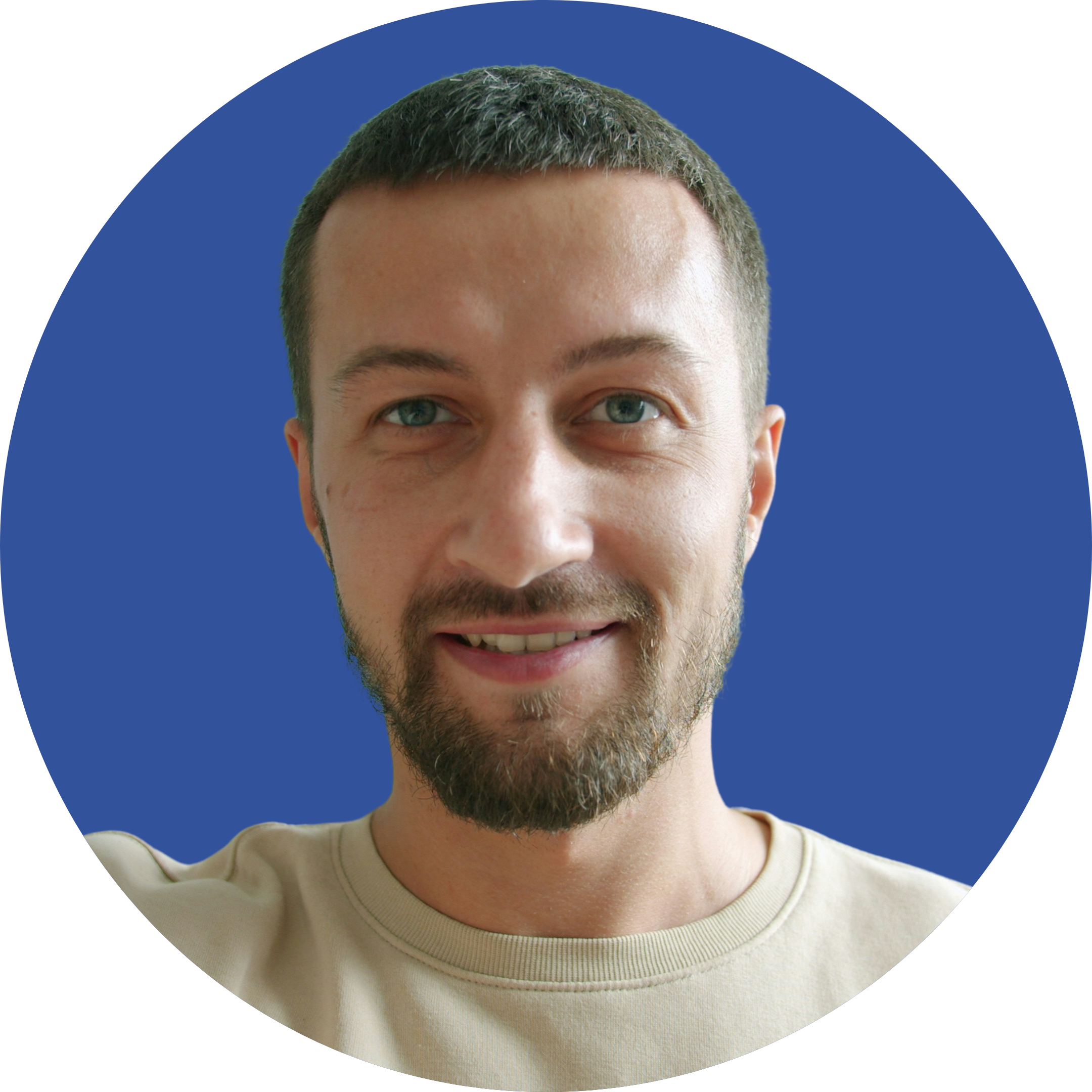 A young man with blue eyes, a beard, and short brown hair, smiling in front of a blue circular background.