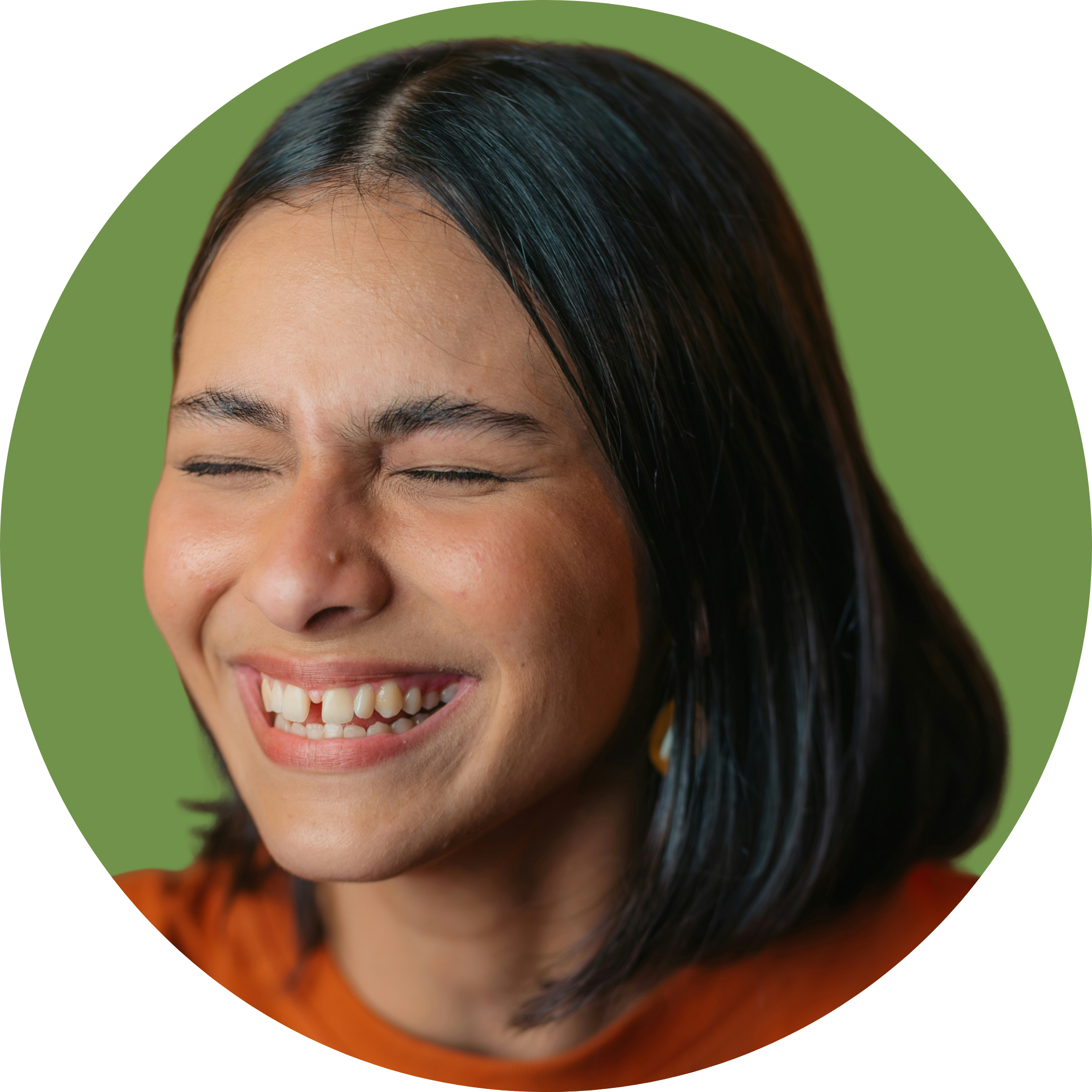 Close-up of a woman with black hair laughing with her eyes closed, wearing an orange top, against a green background.